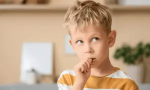 Chłopiec z blond włosami obgryza paznokcie, zastanawiając się, dlaczego dzieci to robią.