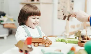 Uśmiechnięte dziecko bawi się drewnianymi zabawkami. Zastanawiasz się, ile wcześniej trzeba zapisać dziecko do żłobka?