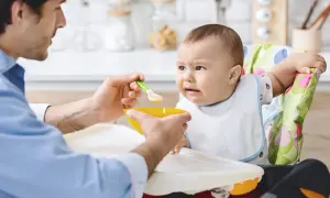 Ojciec karmi dziecko, które nie chce jeść. Czy niemowlę może jeść wątróbkę? Dziecko ma minę wyrażającą niechęć.