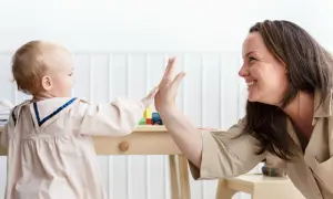Uśmiechnięta opiekunka daje piątkę dziecku. Idealny stosunek, ile dzieci przypada na jedną opiekunkę w żłobku.