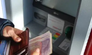 Ręce trzymają portfel i banknoty przy bankomacie. Czy rodzic może wypłacić pieniądze z konta dziecka?