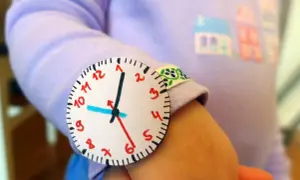 Jak zrobić wskazówki do zegara z papieru? Dziecko nosi na ręce własnoręcznie zrobiony zegarek z papieru.