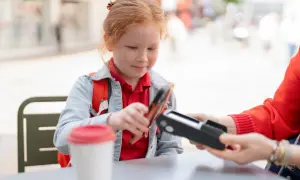 Dziewczynka z rudymi włosami płaci telefonem za kawę. To może być początek nauki, jak zrobic przelew z konta dziecka PKO.