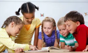 Pięcioro dzieci z zaciekawieniem patrzy na otwartą książkę. To świetny przykład, jak prowadzić zajęcia z dziećmi, angażując ich w naukę.