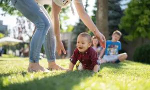 Uśmiechnięty maluch raczkuje na trawie, podczas gdy opiekunka zastanawia się, ile bierze opiekunka do dziecka za noc.