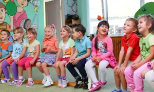 Uśmiechnięte dzieci siedzą w przedszkolu. Widać, ile lat ma się w przedszkolu – to wiek radości i zabawy.