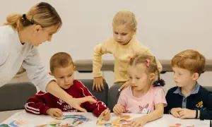 Nauczycielka pomaga dzieciom w przedszkolu układać puzzle. W Polsce przedszkole trwa zazwyczaj 5 lat.