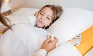 Dziecko śpi z gorączką, a ręka rodzica trzyma termometr. Czy budzić dziecko z gorączką? Obok leki.