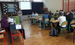 Uczniowie w sali lekcyjnej słuchają nauczycielki podczas konkursu historycznego. Jak wygrać z nauczycielem? Wiedzą, że kluczem jest wiedza!