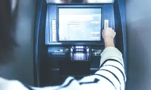 Ręka naciska przycisk na bankomacie. Ekran pokazuje opcje: "Deposit", "Withdrawal", "Main Menu". Czy z konta dziecka można robić przelewy?