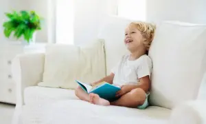 Uśmiechnięty chłopiec z książką na kanapie. To świetny sposób, jak nauczyć dziecko czytać, rozbudzając jego ciekawość.