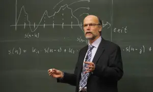 Profesor w garniturze tłumaczy równania na tablicy. Zastanawiamy się, ile godzin ma nauczyciel na etacie, gdy widzi się jego zaangażowanie.