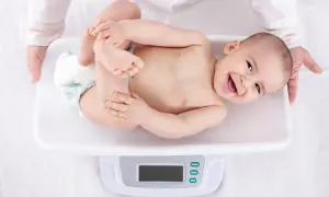 Uśmiechnięte niemowlę na wadze, pokazuje, jak szybko rośnie niemowlę. Rączki i nóżki w górze, radość na twarzy.