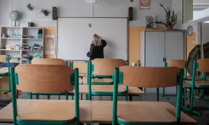 Klasa szkolna z pustymi ławkami. Nauczycielka pisze na tablicy. Zastanawiasz się, ile zarabia pomoc nauczyciela na pół etatu?