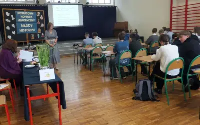 Uczniowie w sali lekcyjnej słuchają nauczycielki podczas konkursu historycznego. Jak wygrać z nauczycielem? Wiedzą, że kluczem jest wiedza!
