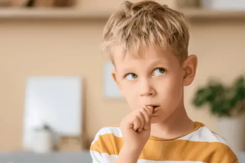 Chłopiec z blond włosami obgryza paznokcie, zastanawiając się, dlaczego dzieci to robią.