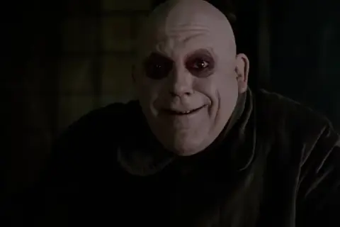 Uśmiechnięty, łysy mężczyzna z ciemnymi kręgami wokół oczu. To wujek Fester z Rodziny Addamsów, znany ze swoich dziwacznych żartów.