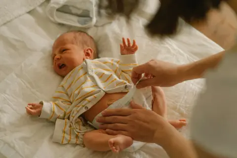 Mama zmienia pieluchę noworodkowi. Jakie pieluchy dla noworodka wybrać, by maluszkowi było wygodnie?