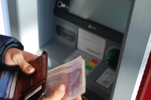 Ręce trzymają portfel i banknoty przy bankomacie. Czy rodzic może wypłacić pieniądze z konta dziecka?