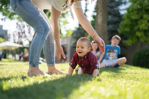 Uśmiechnięty maluch raczkuje na trawie, podczas gdy opiekunka zastanawia się, ile bierze opiekunka do dziecka za noc.