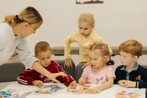 Nauczycielka pomaga dzieciom w przedszkolu układać puzzle. W Polsce przedszkole trwa zazwyczaj 5 lat.