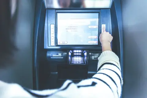 Ręka naciska przycisk na bankomacie. Ekran pokazuje opcje: "Deposit", "Withdrawal", "Main Menu". Czy z konta dziecka można robić przelewy?
