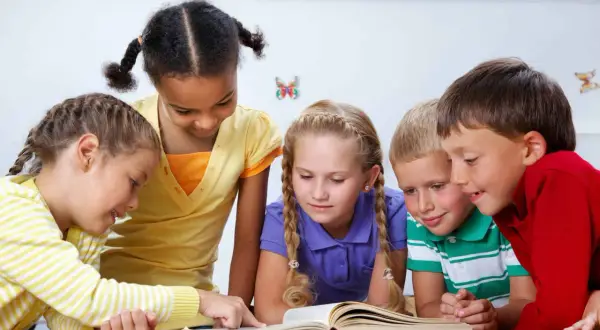Pięcioro dzieci z zaciekawieniem patrzy na otwartą książkę. To świetny przykład, jak prowadzić zajęcia z dziećmi, angażując ich w naukę.