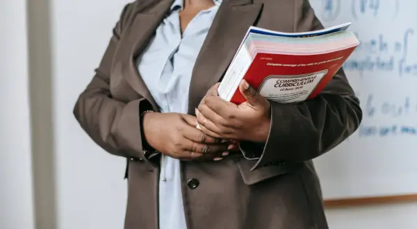 Nauczycielka w brązowej marynarce trzyma książkę "Comprehensive Curriculum". Ile godzin pracuje przedszkolanka? Tyle, ile potrzeba, by przygotować dzieci do życia.
