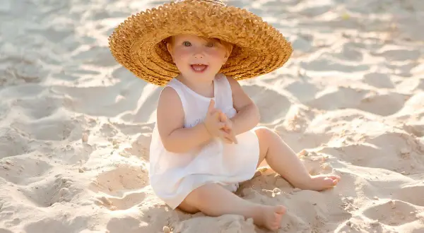 Uśmiechnięte dziecko w słomkowym kapeluszu na plaży. Idealne miejsce, gdzie na wakacje z półrocznym dzieckiem, by cieszyć się słońcem i piaskiem.