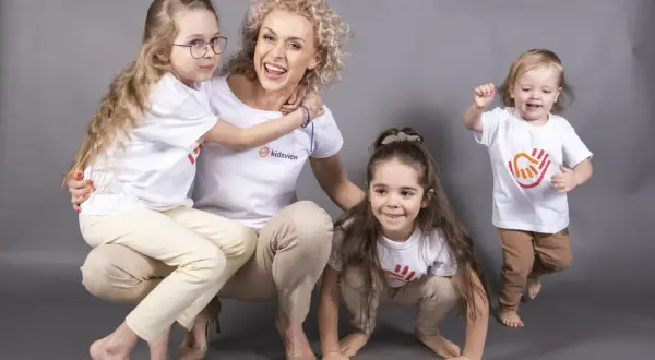 Uśmiechnięta pani z przedszkola prywatnego, otoczona dziećmi. Ile godzin pracuje nauczyciel w przedszkolu prywatnym? Tyle, ile potrzeba, by dać im radość!
