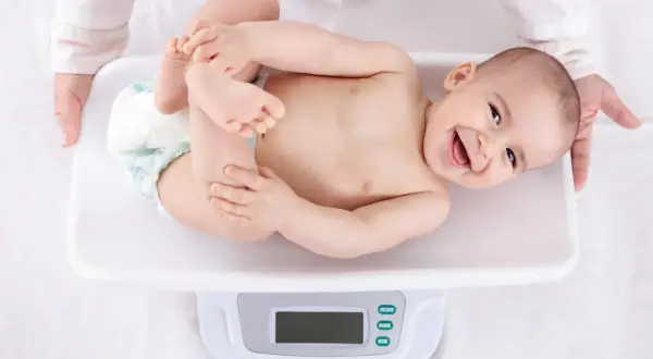 Uśmiechnięte niemowlę na wadze, pokazuje, jak szybko rośnie niemowlę. Rączki i nóżki w górze, radość na twarzy.