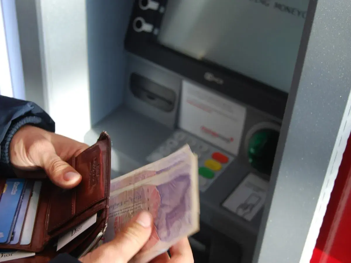 Ręce trzymają portfel i banknoty przy bankomacie. Czy rodzic może wypłacić pieniądze z konta dziecka?