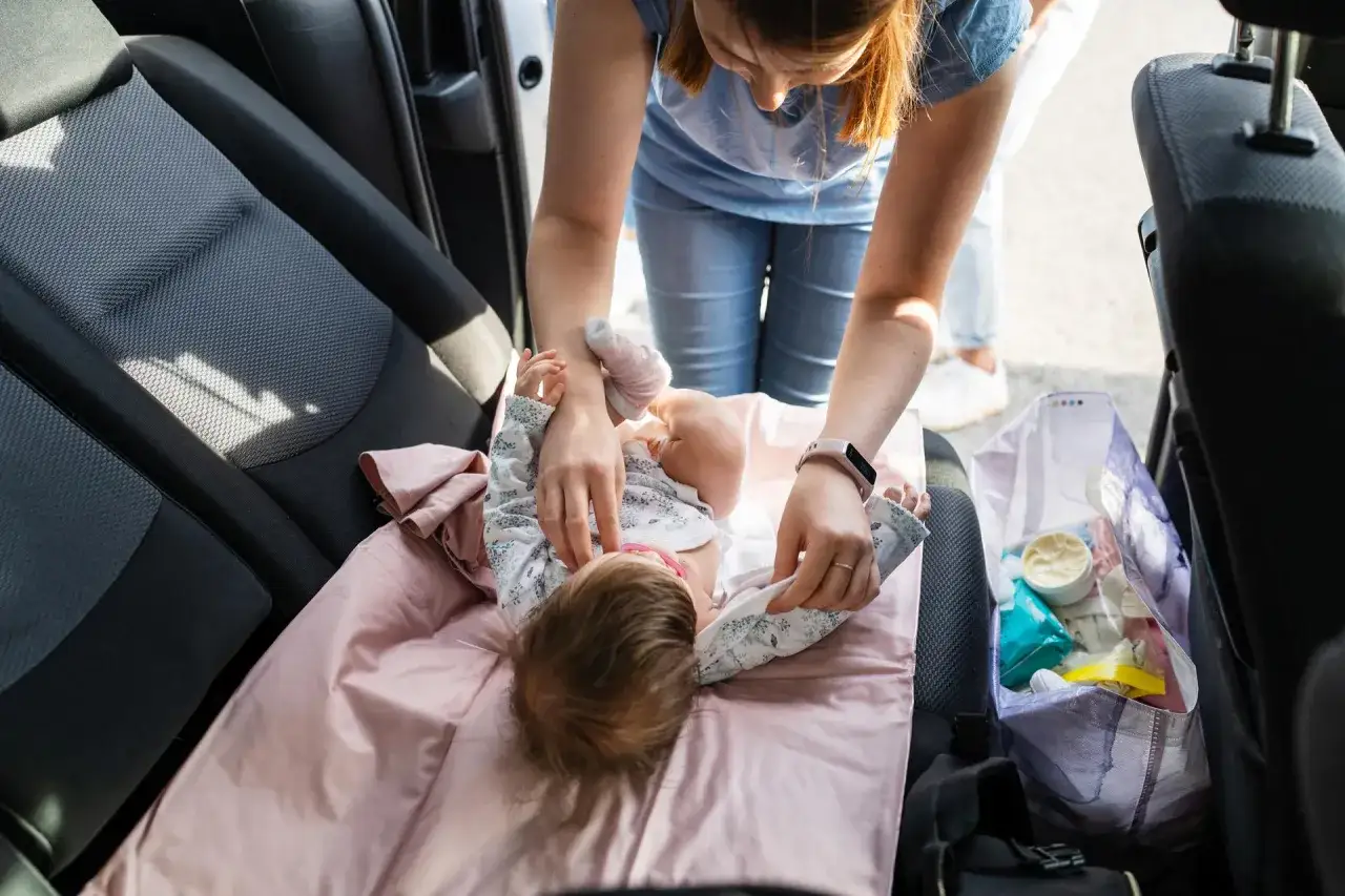 Mama zmienia pieluszkę dziecku w samochodzie, zastanawiając się, kiedy zmieniać pieluszkę przed czy po karmieniu.