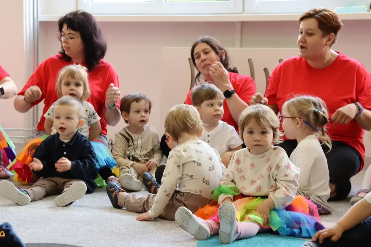 Wesoła grupa dzieci w żłobku, siedząca na dywanie z opiekunkami.