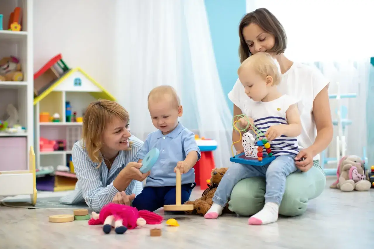 Dwie opiekunki bawią się z dwójką dzieci w grupie żłobkowej. Wszyscy są uśmiechnięci i zaangażowani w zabawę.
