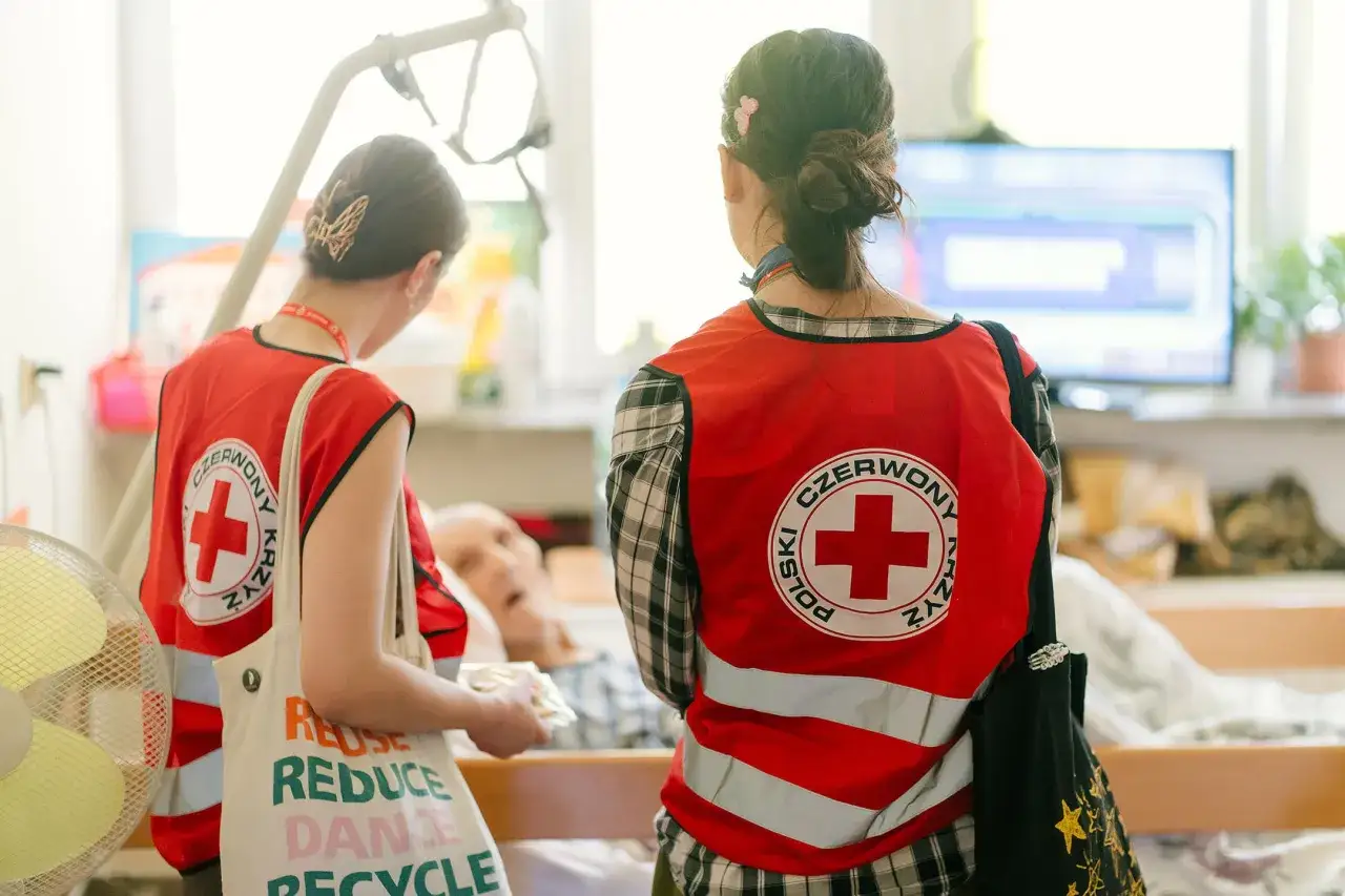 Dwie wolontariuszki PCK w czerwonych kamizelkach opiekują się pacjentem. Zastanawiasz się, ile kosztuje opiekunka z PCK?