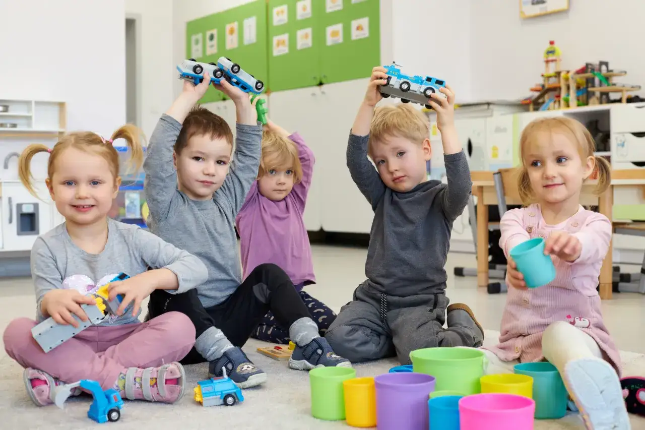 Dzieci w przedszkolu, w wieku od 3 do 5 lat, bawią się samochodzikami i kolorowymi kubeczkami.