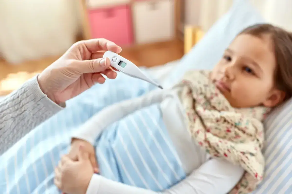 Chora dziewczynka w łóżku, mama mierzy jej temperaturę. Szukamy co na przeziębienie dla rocznego dziecka.