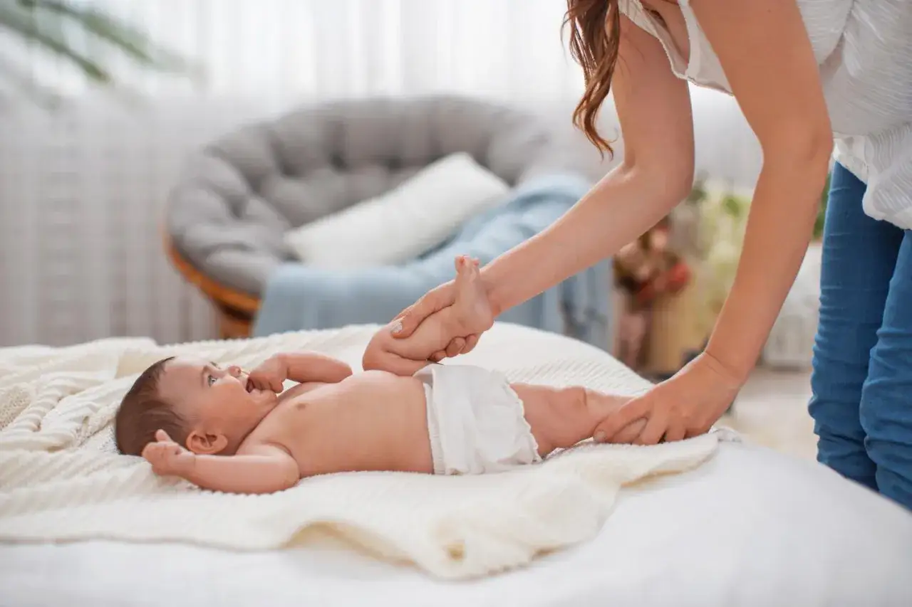Mama delikatnie podnosi nóżkę dziecka, zastanawiając się, kiedy zmieniać pieluszkę przed czy po karmieniu.