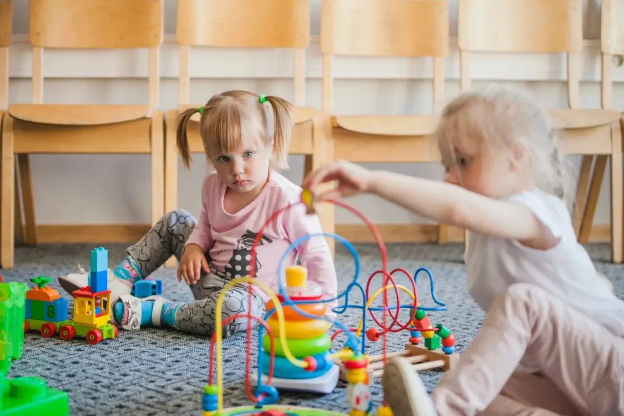 Dwie dziewczynki bawią się klockami i zabawkami edukacyjnymi. Czy żłobek to dobry pomysł? Dzieci uczą się i rozwijają.