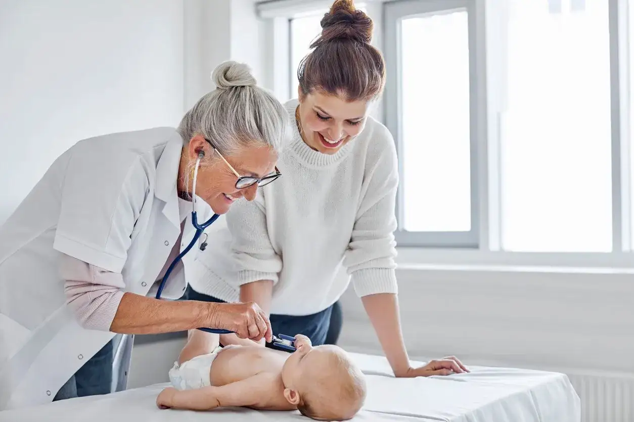 Lekarka bada niemowlę, a mama obserwuje. Szuka się informacji: co na biegunkę u rocznego dziecka -- domowe sposoby.