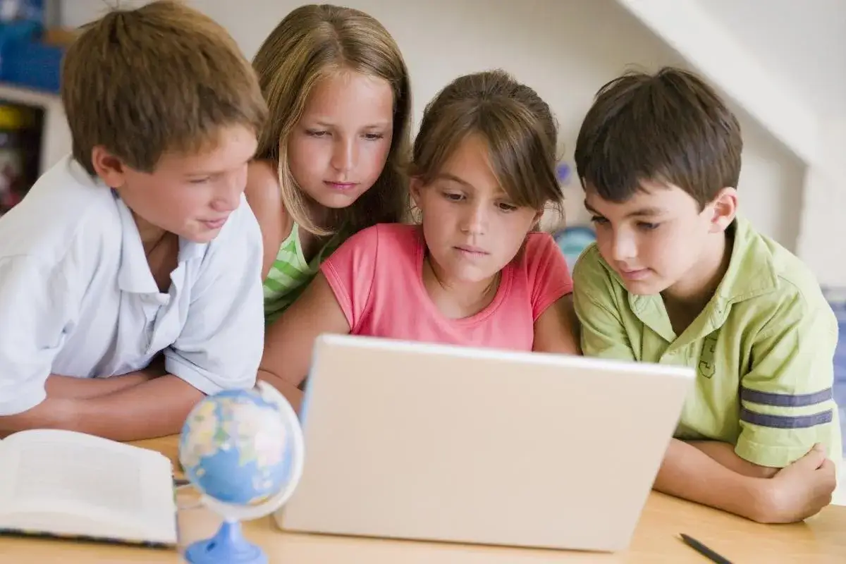 Dzieci uczą się, jak działa aplikacja, gdzie jest dziecko, na laptopie. Obok leży globus i otwarta książka.