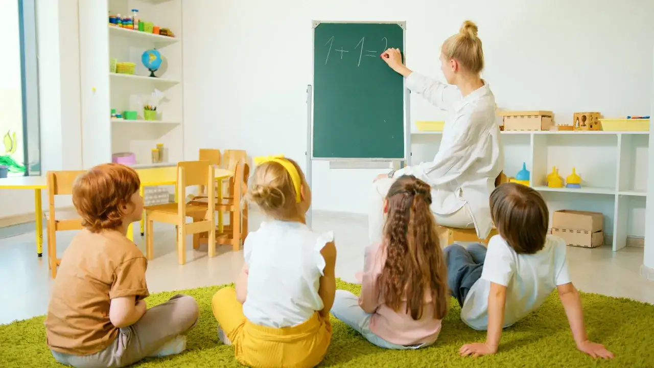 Nauczycielka w przedszkolu prywatnym pisze na tablicy