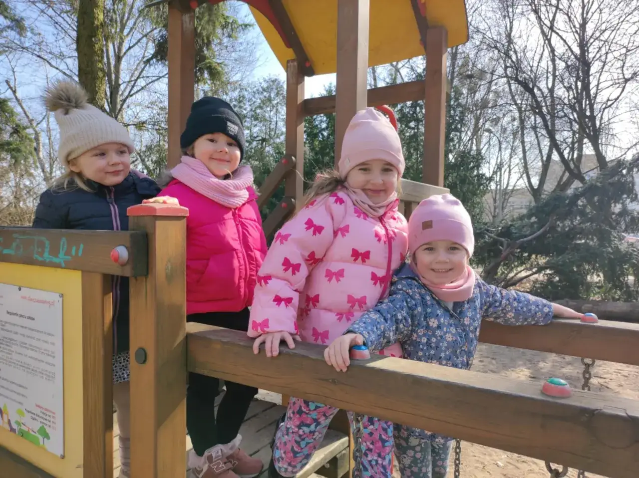 Cztery uśmiechnięte dziewczynki na placu zabaw. W Polsce przedszkole trwa zazwyczaj 5 lat, od 3 do 6 roku życia.