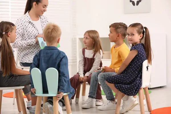 Nauczycielka czyta dzieciom książkę. Grupa przedszkolna liczy 6 dzieci.