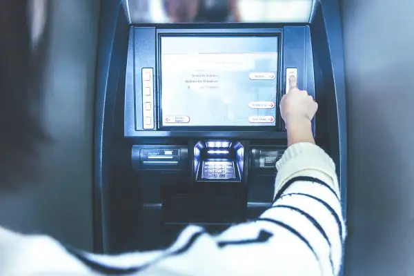 Ręka naciska przycisk na bankomacie. Ekran pokazuje opcje: "Deposit", "Withdrawal", "Main Menu". Czy z konta dziecka można robić przelewy?