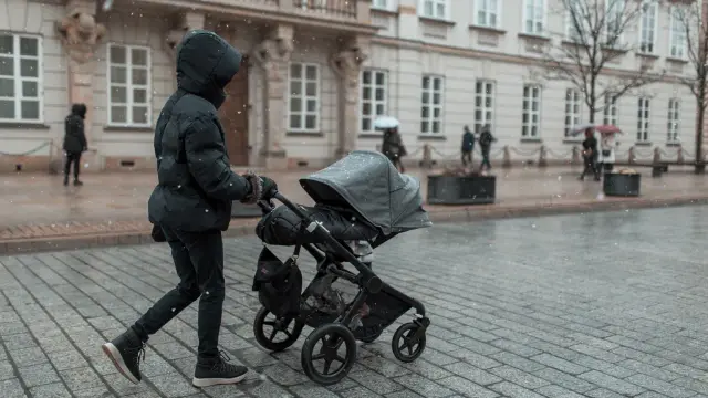 Osoba w zimowej kurtce pcha wózek po ośnieżonym bruku. Czy z temperaturą 38 można wychodzić na dwór z dzieckiem?